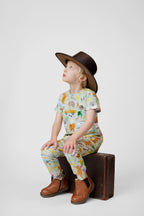 Child wearing Summer Down Under organic cotton kids outfit by Pebble and Poppet sitting on vintage suitcase wearing wide brim Australian outback hat. Designed and made in Australia.