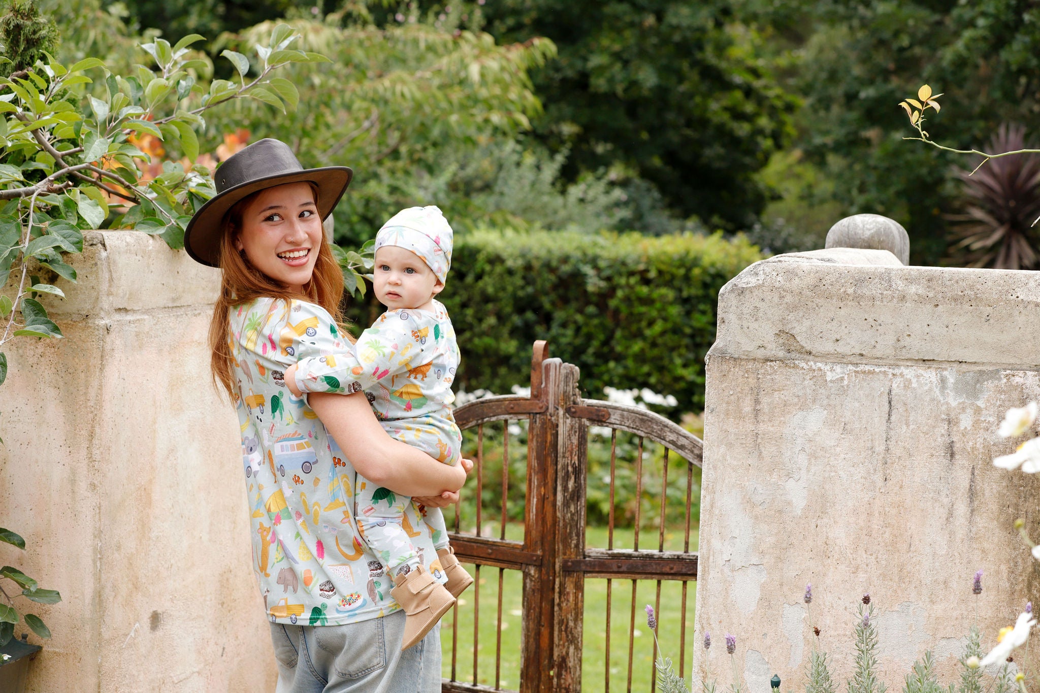 Mother and baby wearing matching Summer Down Under Australian print organic cotton outfits in a garden setting.