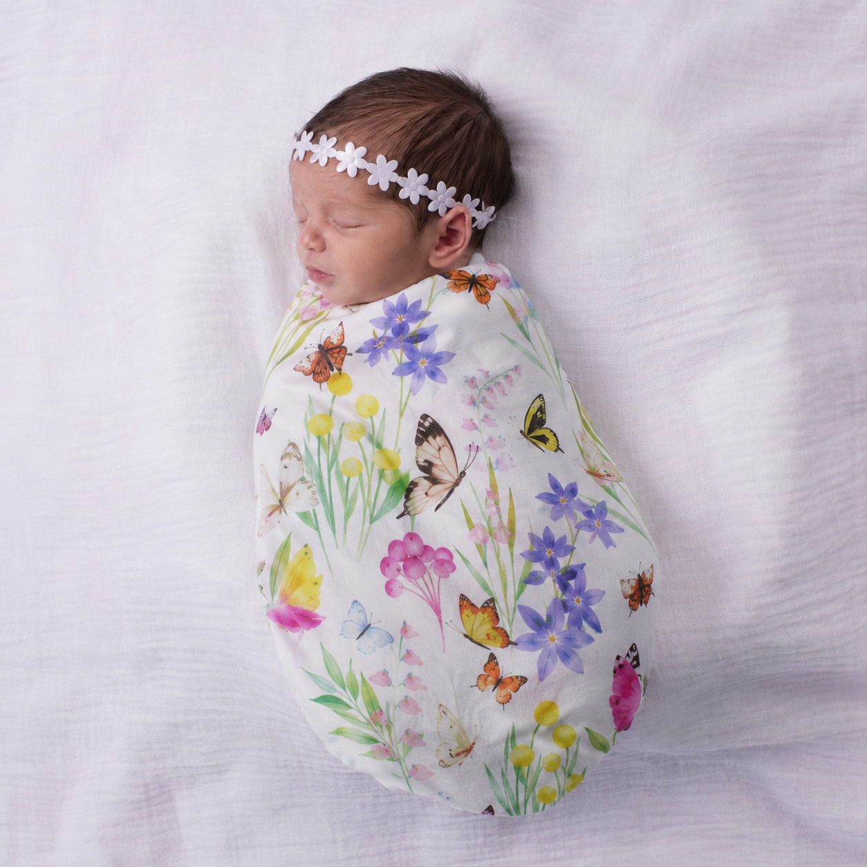Sleeping newborn baby wrapped in the Butterfly Flora organic bamboo swaddle by Pebble and Poppet, featuring Australian wildflowers and butterflies illustrated by Christie Williams