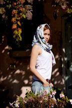 Woman wearing a soft Australian bird print scarf outdoors in warm sunlight surrounded by vines and flowers.